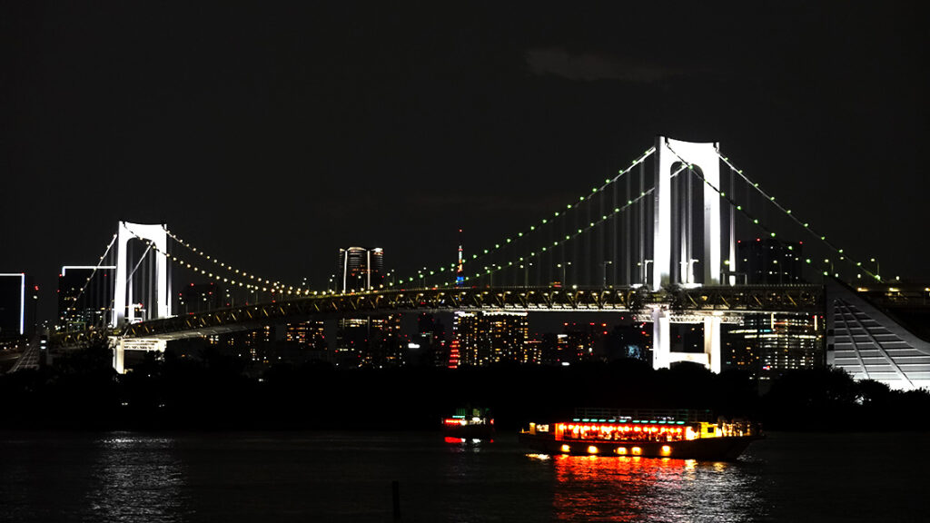 El puente Rainbow Bridge iluminado de noche con la Torre de Tokio de fondo en la bahía.