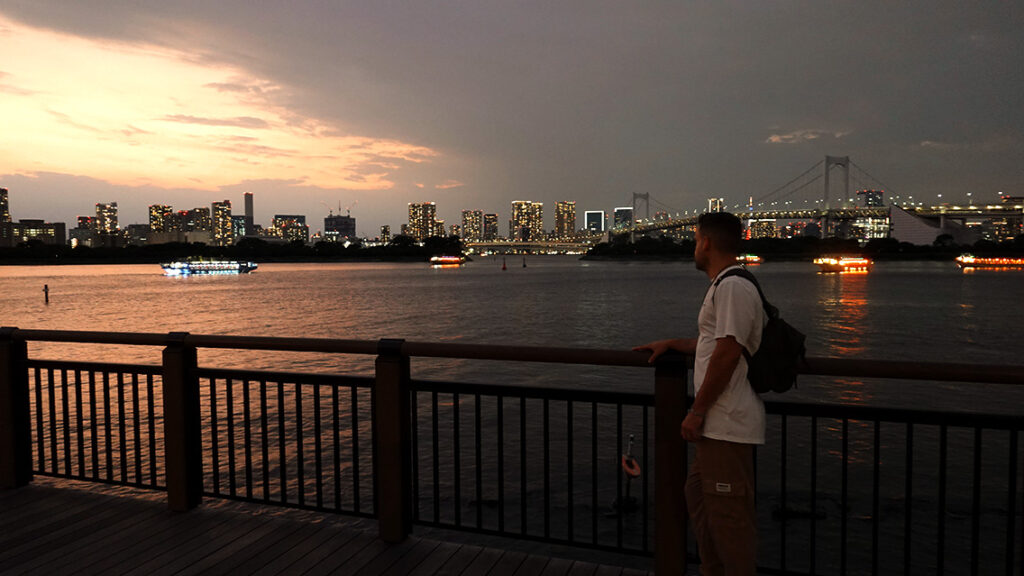 Joan en la playa del parque de Odaiba durante el atardecer con el Rainbow Bridge de fondo.