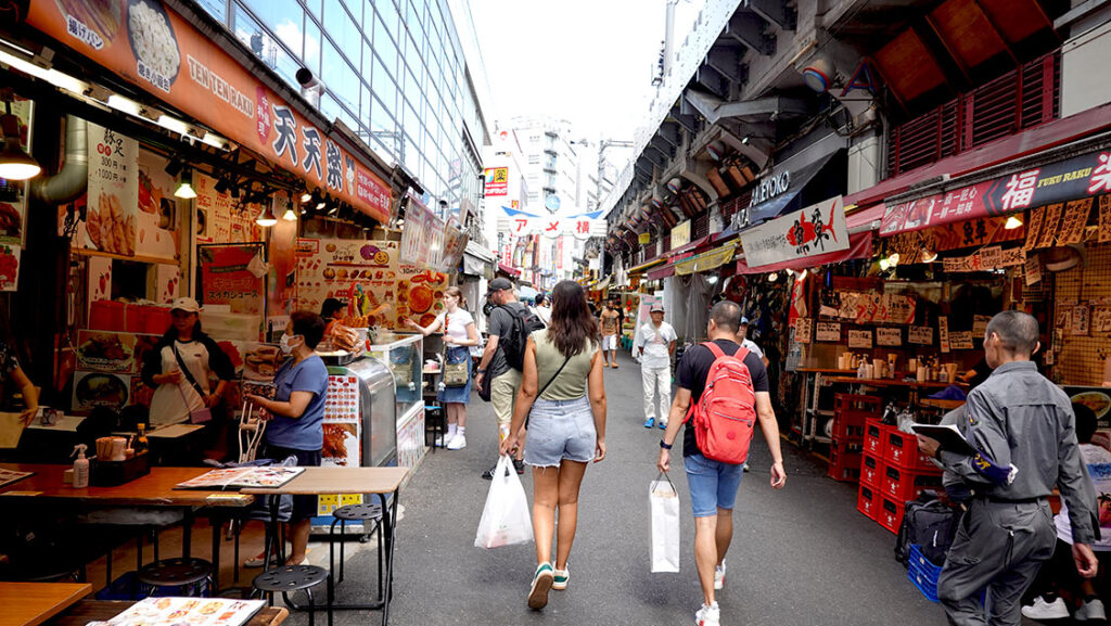 Noelia paseando por la concurrida calle Ameyoko en Ueno con puestos de comida callejera, restaurantes y tiendas de ropa.
