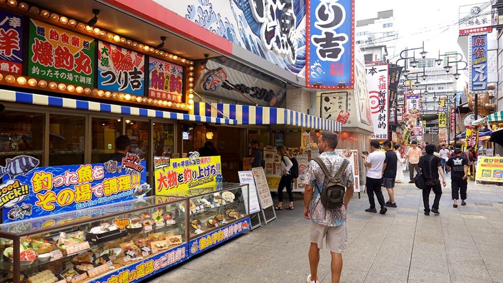 Joan caminando por la calle principal del barrio de Shinsekai en Osaka con la torre Tsūtenkaku al fondo.