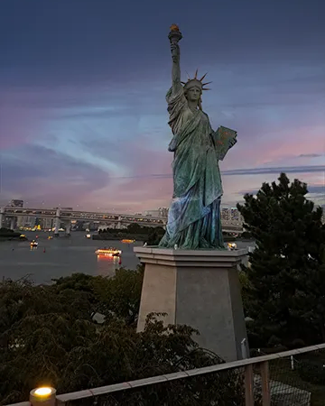 Réplica de la Estatua de la Libertad en Odaiba frente al puente Rainbow Bridge iluminado.