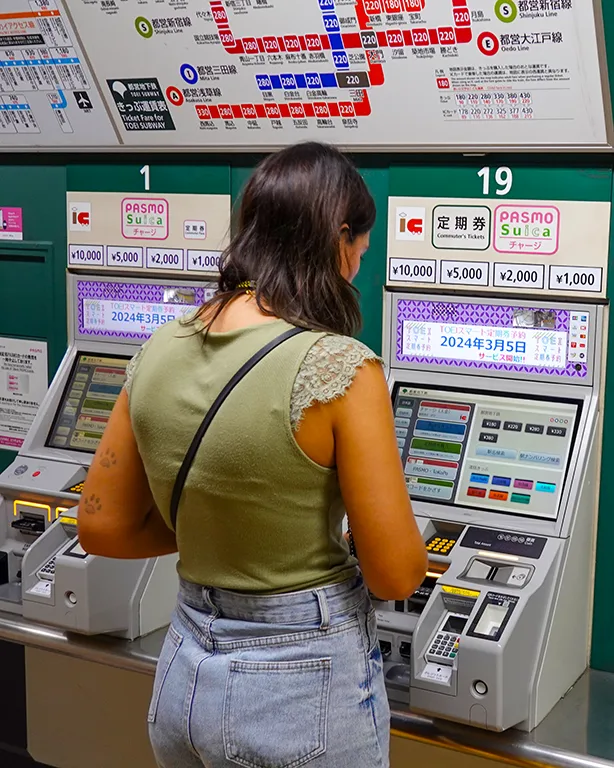 Viajera comprando un billete en las máquinas del metro de Tokio con el mapa de tarifas de colores al fondo
