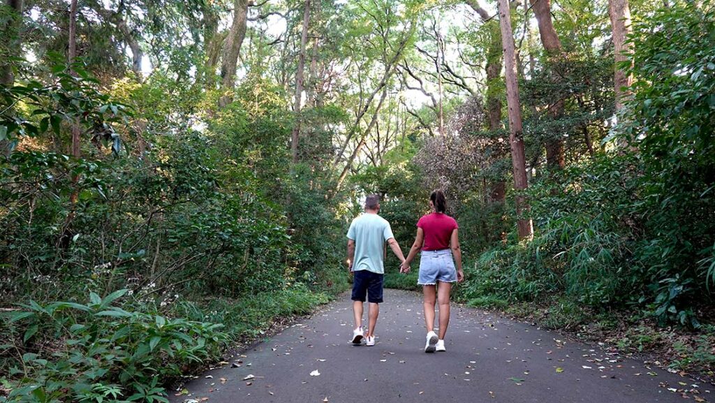 Dos viajeros caminando por los senderos arbolados del Parque Yoyogi en Tokio un día soleado.