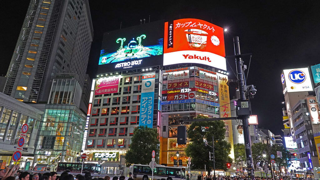 Edificios iluminados y pantallas gigantes alrededor del cruce de Shibuya de noche.
