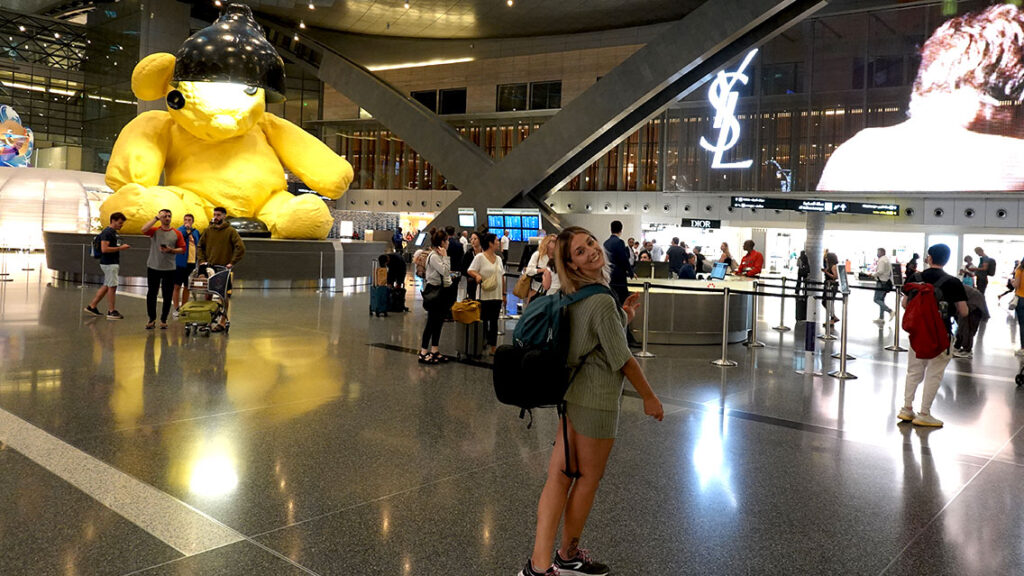 Noelia sonriendo junto al famoso osito gigante amarillo en el aeropuerto de Doha.