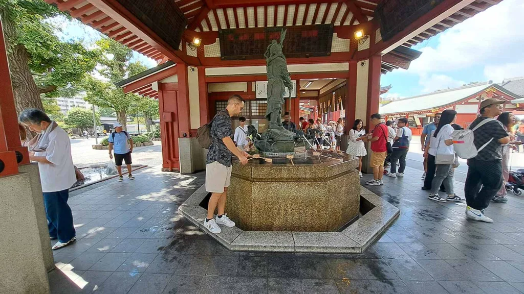 Joan realizando el ritual de purificación con el cazo de agua en la fuente Temizu del templo.