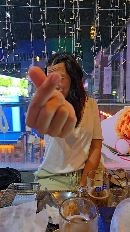 Noelia haciendo el dedo coreano mientras come pollo frito en el barrio universitario de Seúl