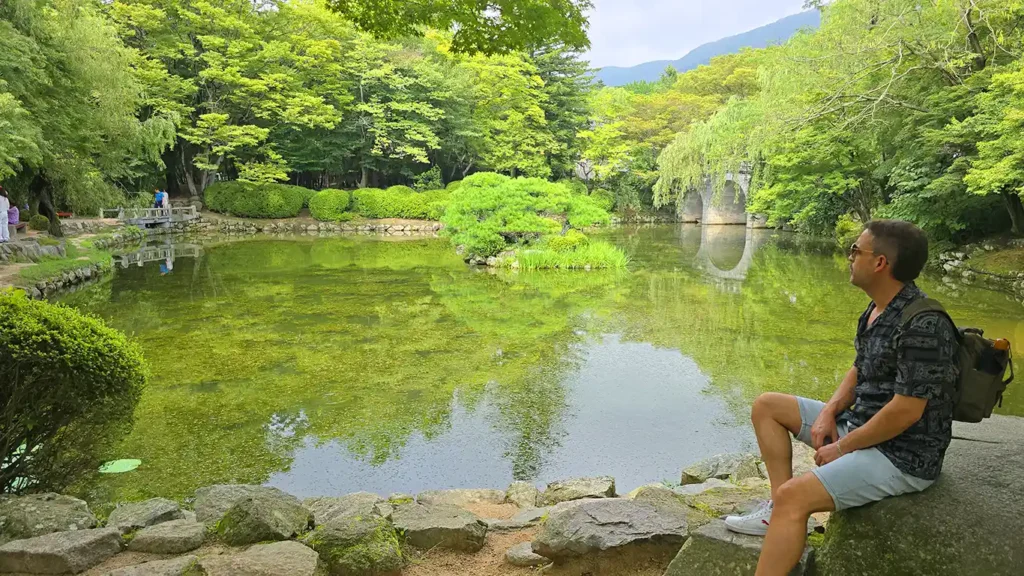 Joan sentado en el Estanque Banya Teonji Pond con el puente de entrada al templo de fondo