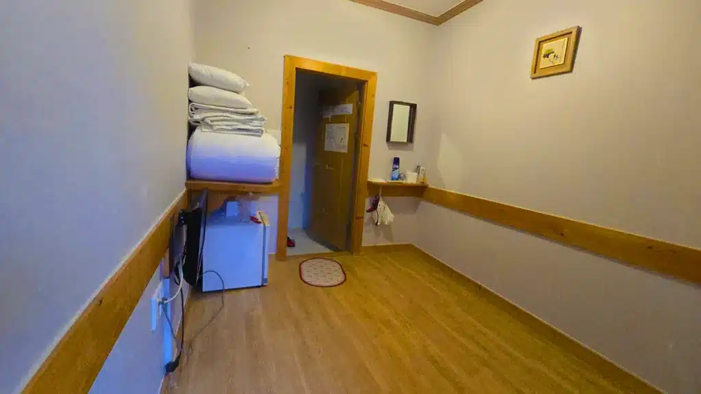 Interior de una habitación de una casa Hanok, hay una nevera, futones y la puerta al baño