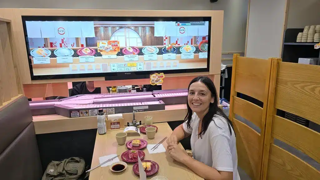 Noelia comiendo sushi en un restaurante y una cinta donde traen la comida de fondo