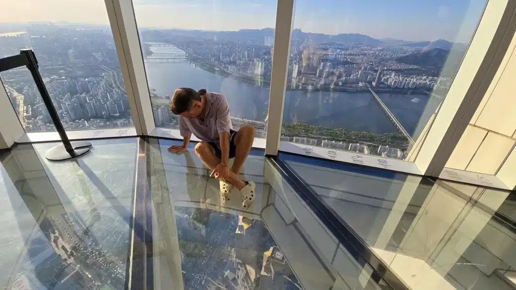 Joan sentado en el suelo de cristal en Seoul Sky, el 6o mirador más alto del mundo