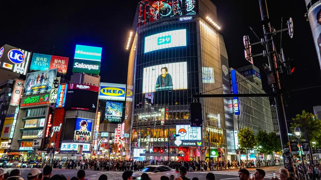 Cruce de Shibuya por la noche con pantallas y edificios iluminados