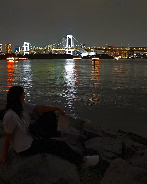 Noelia paseando por la arena de la playa artificial Odaiba Beach de noche con luces de fondo.