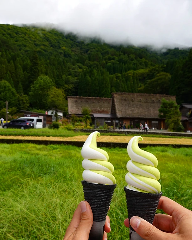 Dos helados de crema de té verde matcha con las casas tradicionales de paja gassho-zukuri de fondo en Shirakawago